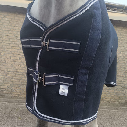 Navy blue horse blanket with white trim on a horse, against a brick wall background.