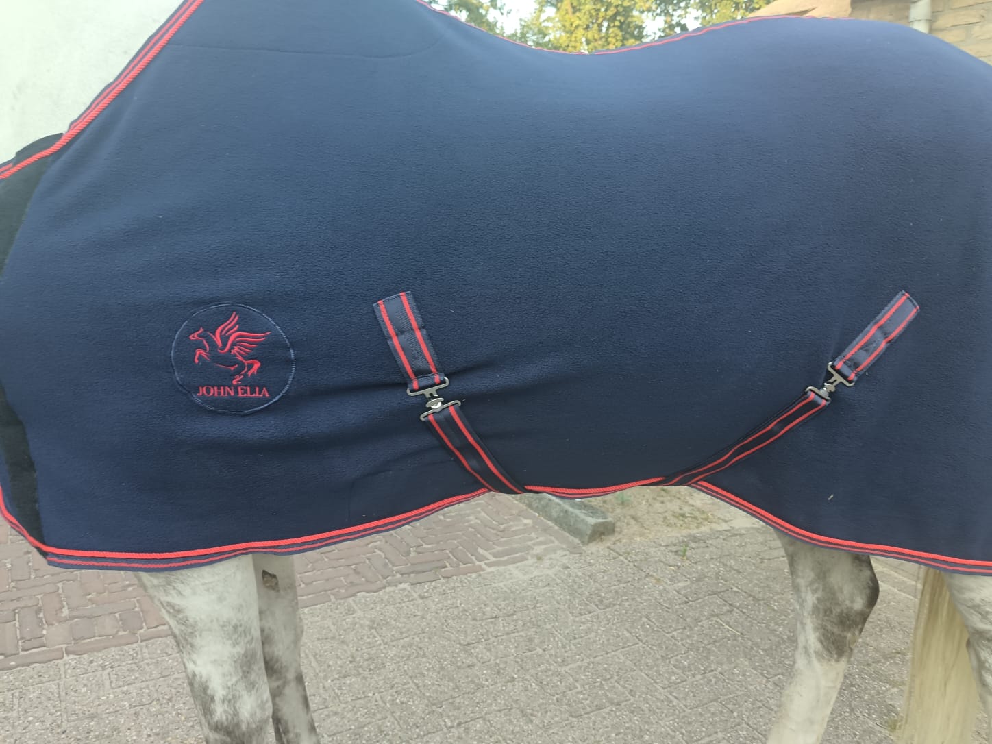 Navy blue horse blanket with red trim and a brand logo on a horse.